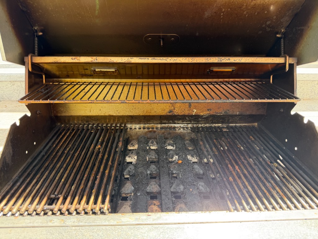 Gas grill interior with heavy grease and carbon buildup on grates and firebox before cleaning