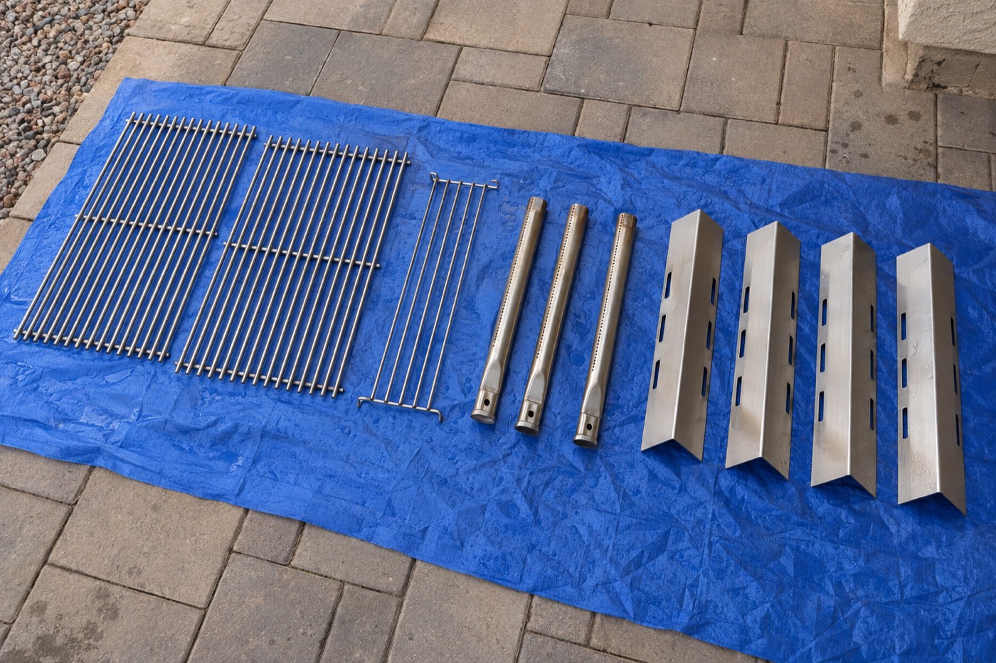 Cleaned stainless grill grates, burners, and heat plates laid out on a tarp